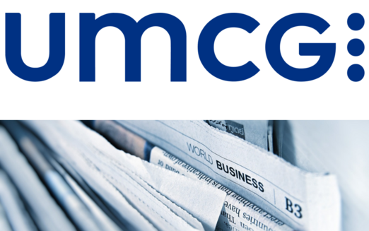 UMCG logo above a close-up stack of newspapers with “World Business” visible.