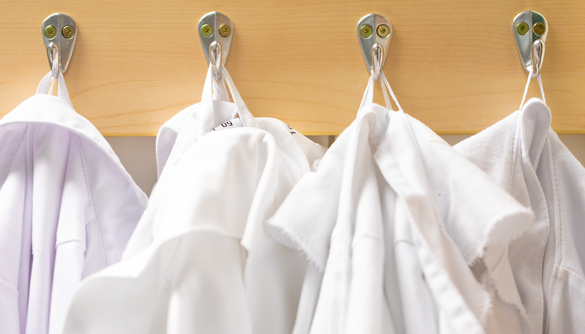 White laboratory coats hanging on hooks, representing clinical and research work in a biomedical research environment.